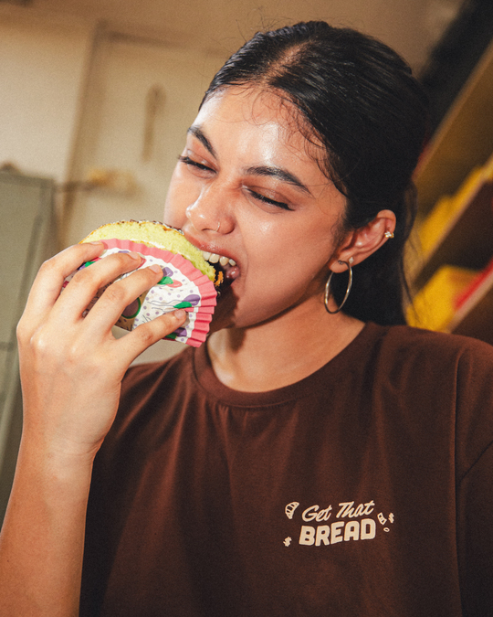 woman eating a piece of bread in a brown graphic t shirt that says get that bread