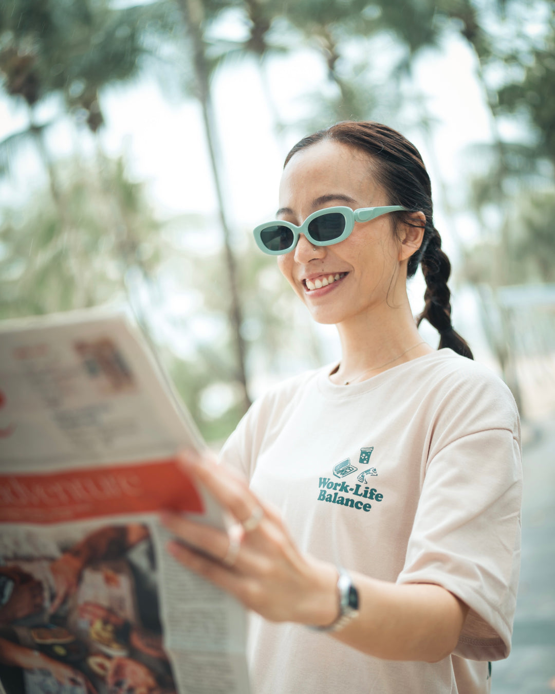 woman in funky shades wearing a graphic t shirt reading a newspaper