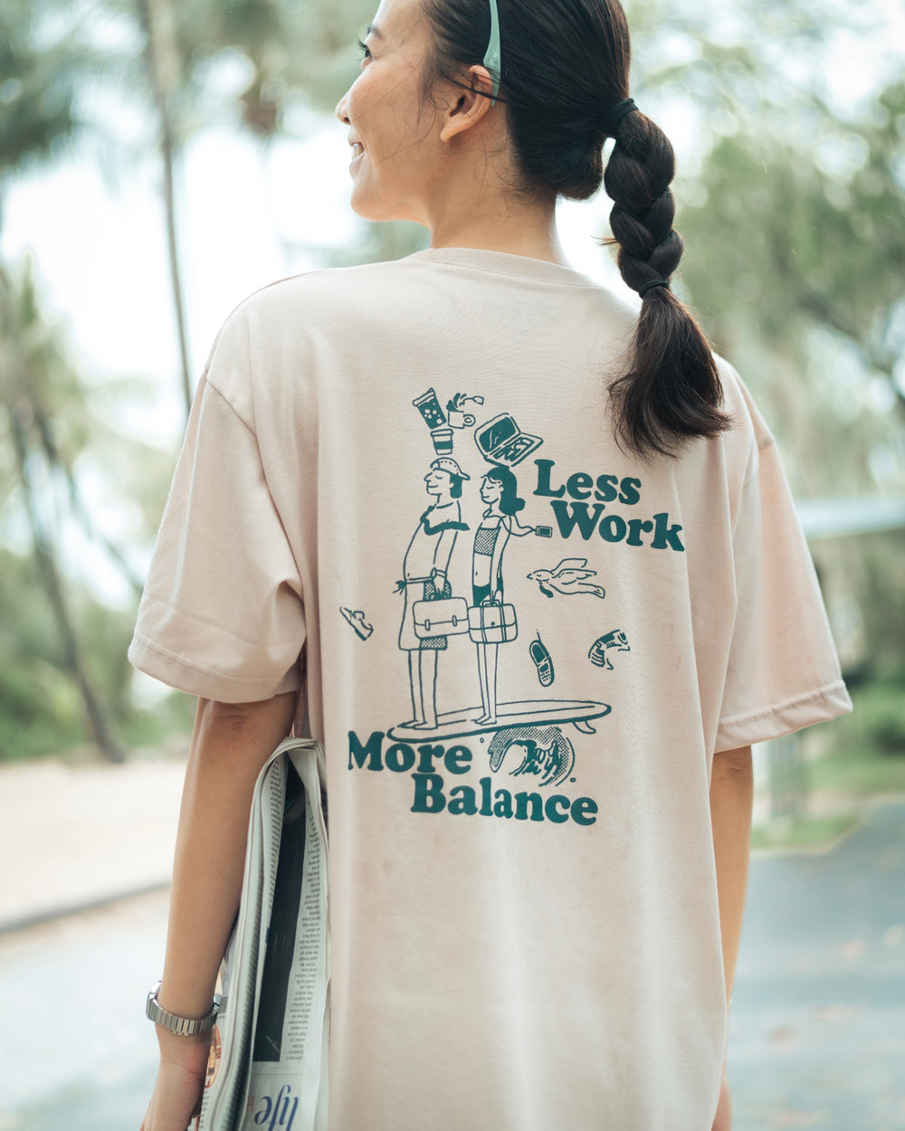 lady wearing a graphic t shirt saying work life balance on the back holding newspaper