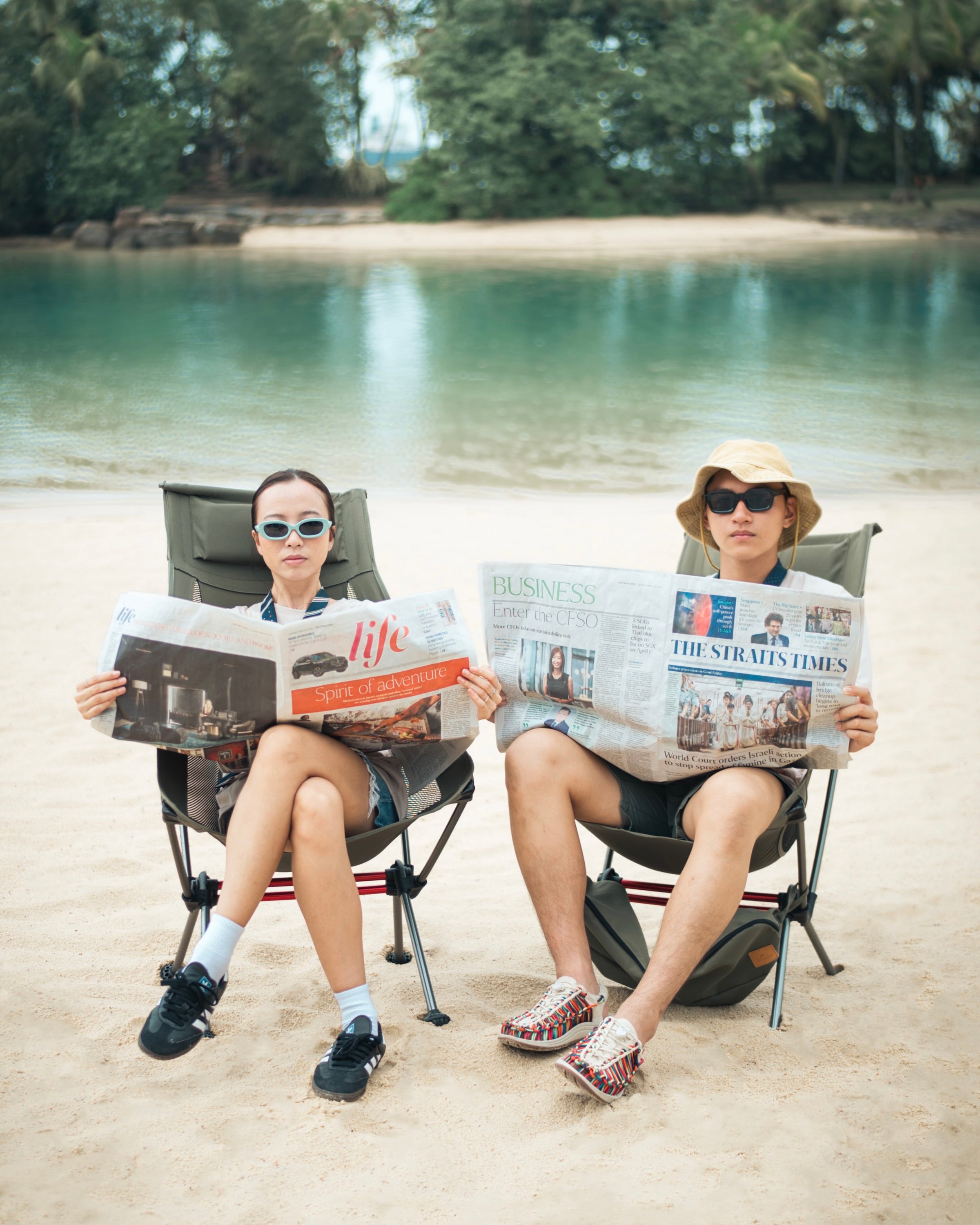 one woman and one man sitting on the beach reading newspaper